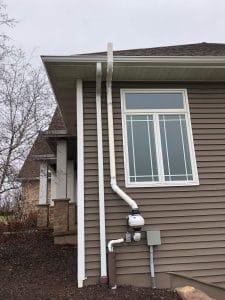 Exterior view of a radon mitigation system with a vent pipe and fan installed on the side of a residential home"